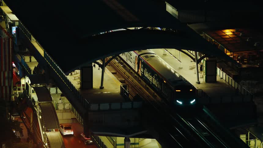 Passenger train travels on an elevated track through a tunnel paralleling a busy city street at night