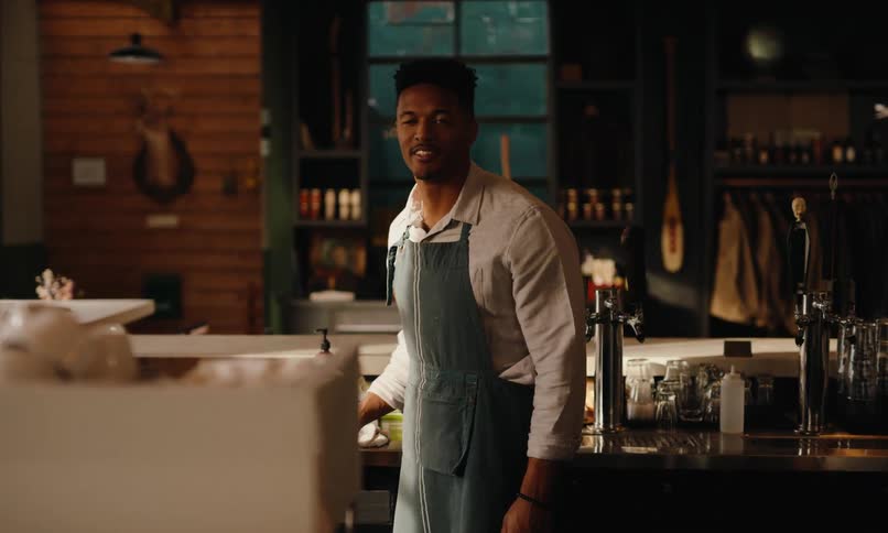 A barista works behind the counter of a rustic coffee shop with wooden shelves filled with various items