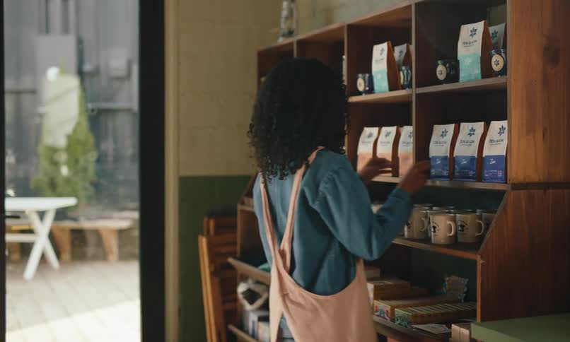 A female multi-racial worker is straightening the products on the shelves in the cafe
