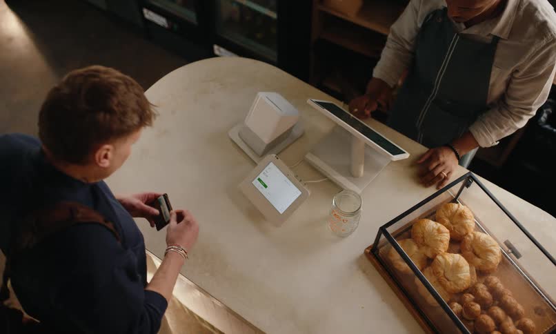 A person places an order at a bakery counter and pays using a credit card