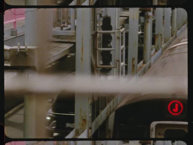 A train traveling inside a steel tunnel with cars moving along the road beside the train tracks during daylight