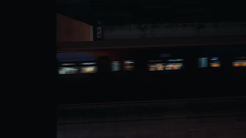 Dimly lit train cars moves through the darkness its illuminated windows revealing blurred interiors