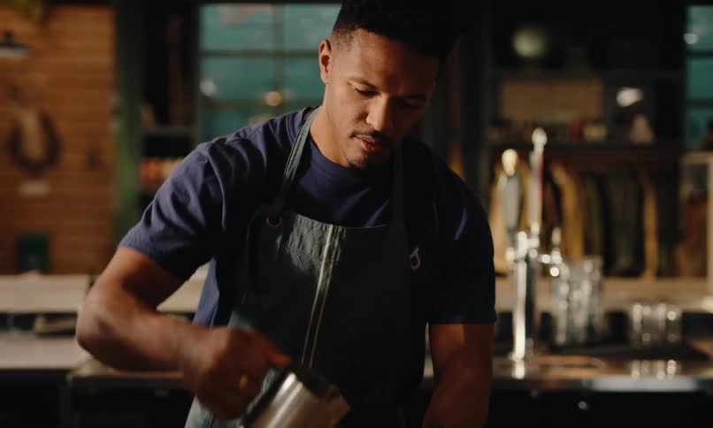 Man in apron in a coffee shop preparing a drink