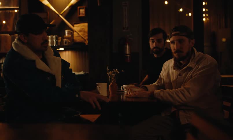 A group of people seated at a wooden table in a dimly lit cafe react with surprise to something falling rising to assist