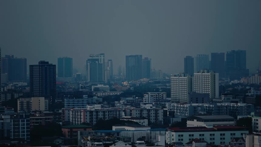 A cityscape under a dusky sky reveals a mix of low and highrise buildings with scattered lights illuminating the urban scene