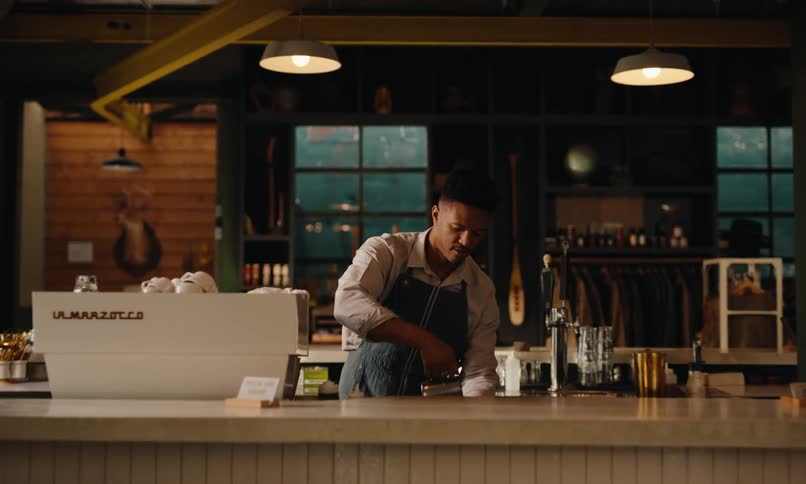 A barista prepares a drink behind a counter in a warmly lit caf with wooden and industrial decor