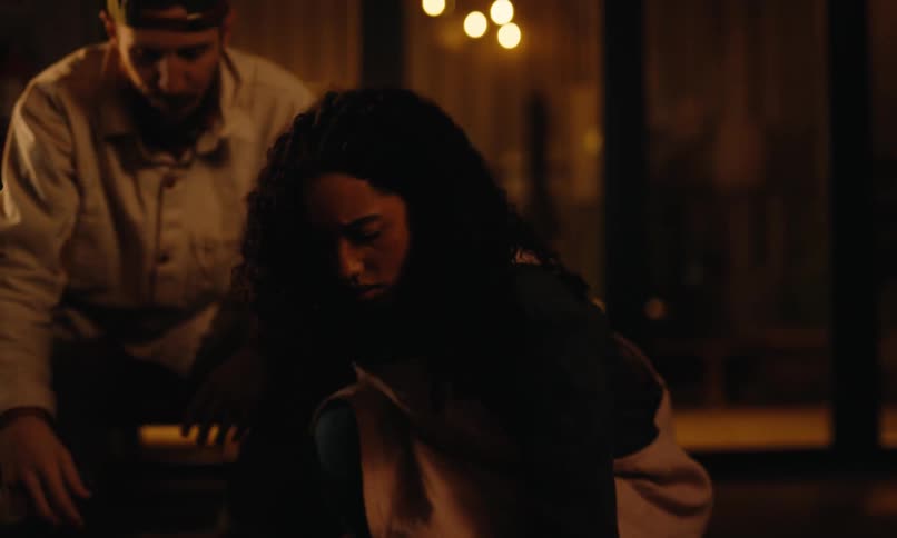 A young black woman holds and accidentally drops a black bowl on the floor while picking up some items a man seeing this offers to help her as she looks at him in surprise
