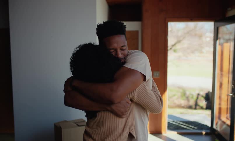 Two people embrace inside a room with an open door leading outside