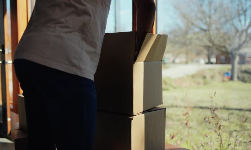 Man unpacking items from a box sitting next to large windows of a house
