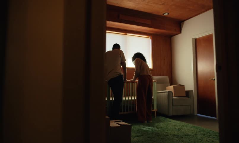 A man and woman stand over a crib talking and touch the crib