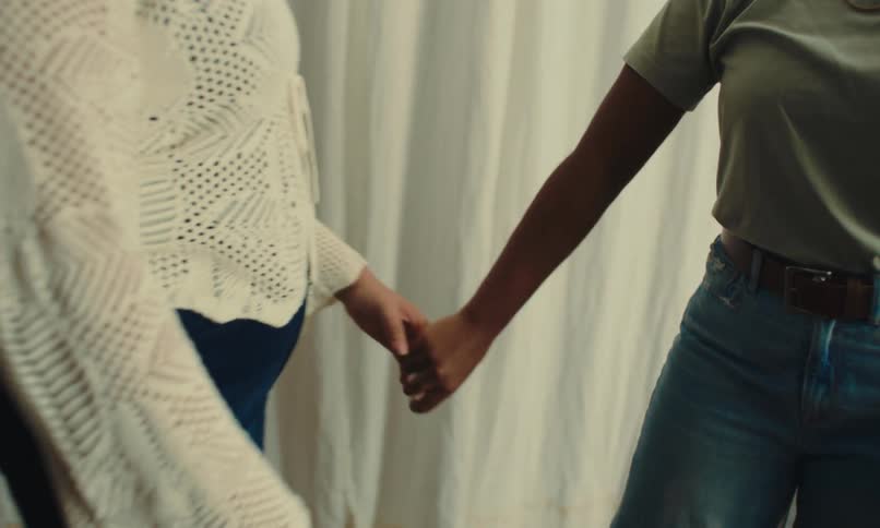 Two women holding hands who are approaching and one of them is wearing a white outfit with several holes