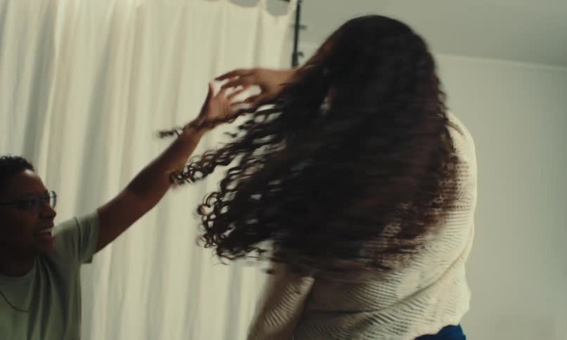 Woman twirls another woman in order to see her outfit while sitting near a stand alone backdrop curtain