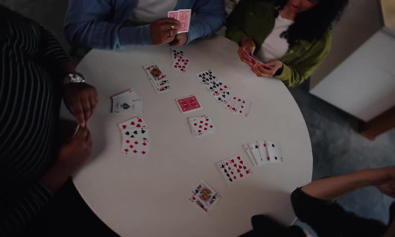 Freinds sitting around a small round dining table playing a card game