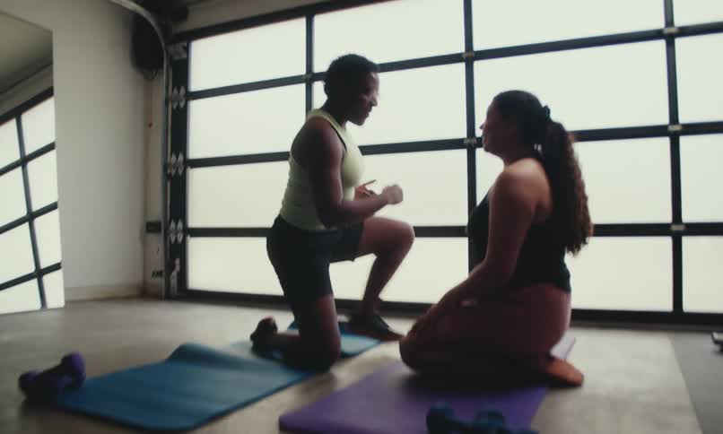 A woman helps her friend up in the gym