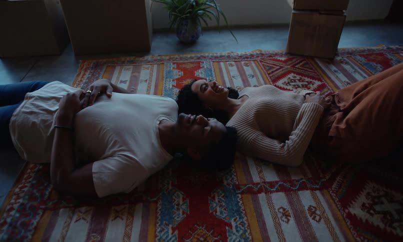 A man and a woman lying on a colorful rug talking while looking up happily