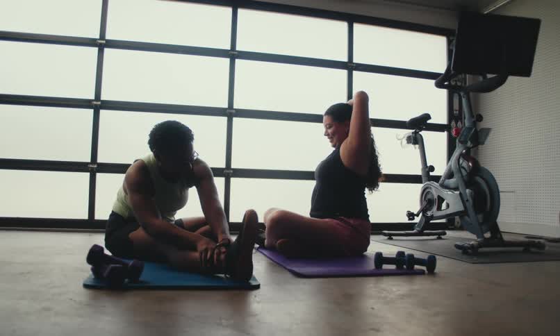 Two women are stretching on exercise mats in a workout room