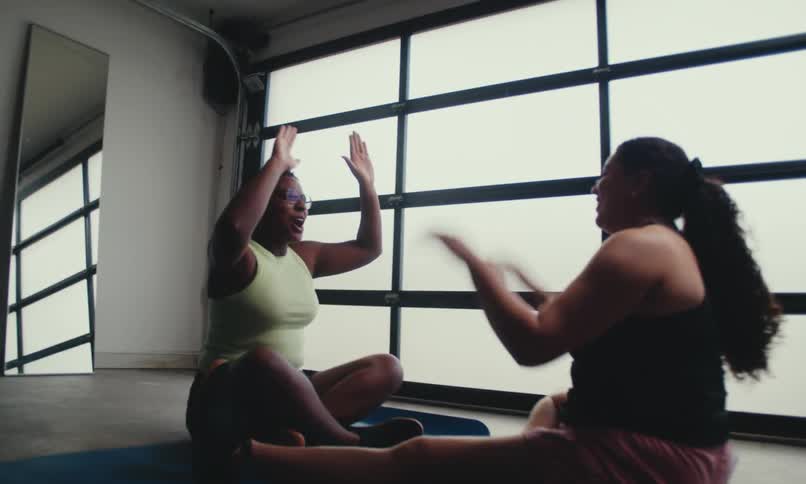 Two women stretch in a bright spacious room preparing to exercise on mats