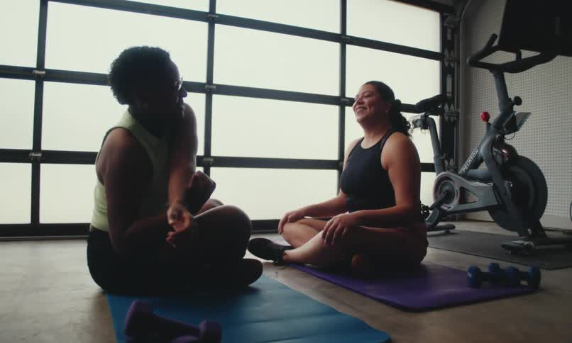 Two women sitting in a gym environment stretching their bodies