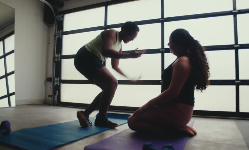 Two women rise from their yoga mats after completing a stretching routine facing each other in a serene setting