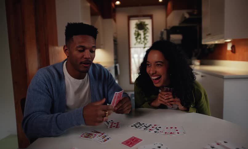 A diverse group of friends laughs and plays cards together around a table indoors