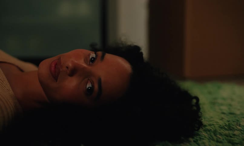 The face of a young woman who is lying on the floor looking up then looks to the side smiling while talking