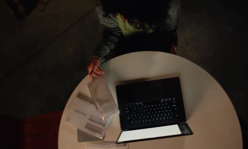 Distressed woman sitting at a table with an open laptop and looking at letters and bills