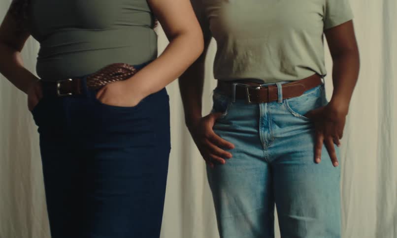 Body of two women together with jeans and brown leather belt