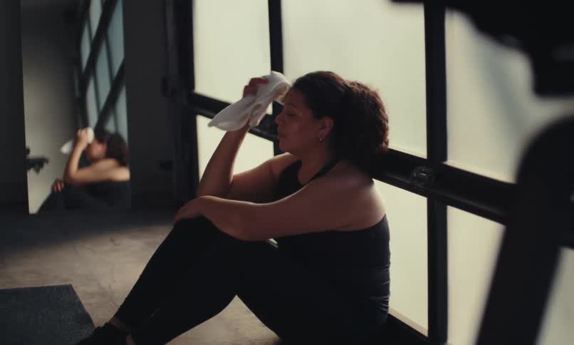 A woman sits and rests while wiping sweat off with a towel