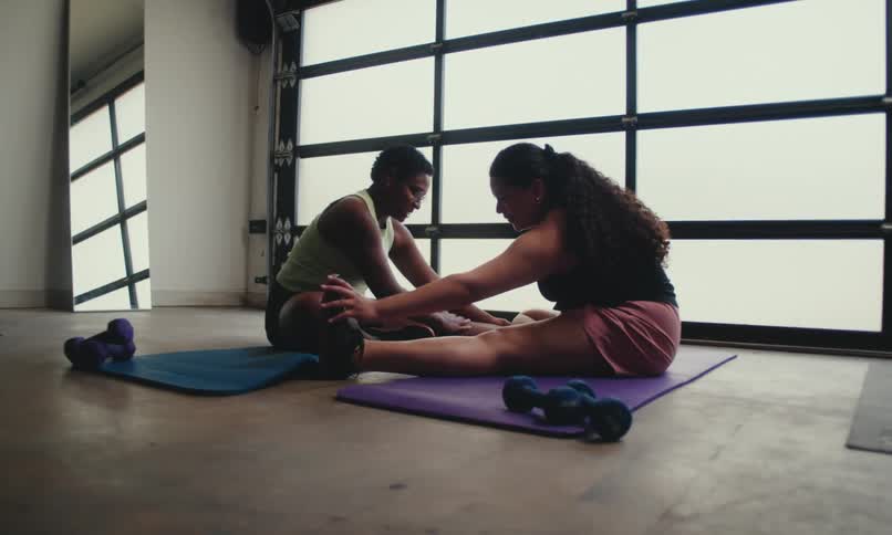 Two women are on yoga mats doing stretches