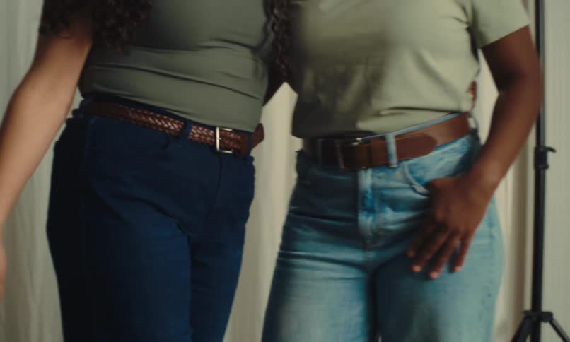 Two women wearing jeans and t shirts side hug while standing in front of a photography backdrop on a photography set