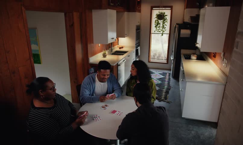 Friends hanging out laughing playing cards on a small round dining table in the kitchen