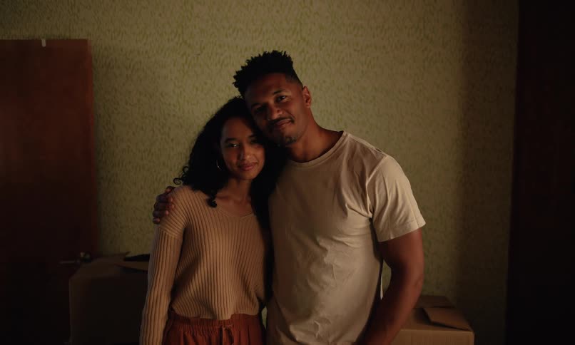 A couple hugging in a room surrounded by packed boxes suggesting a moving or unpacking scenario in a brightly lit space