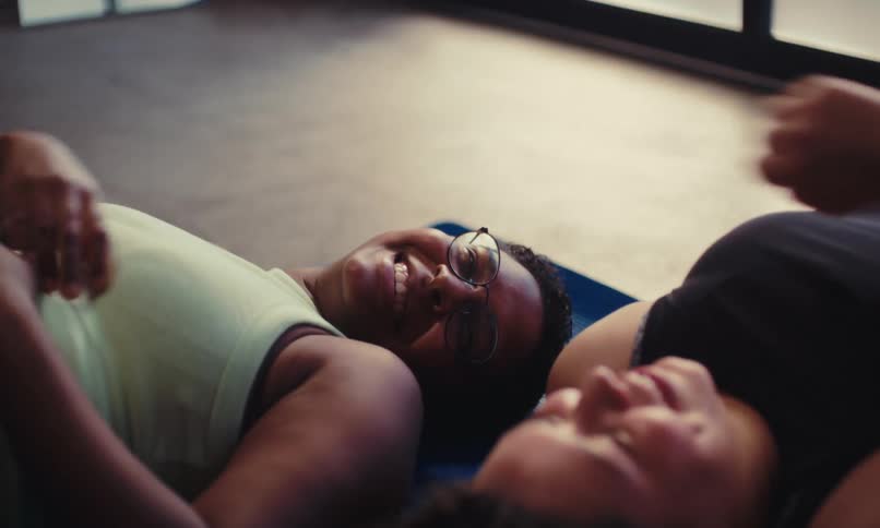 Two people lie on yoga mats in a brightly lit space relaxing and celebrating post exercise