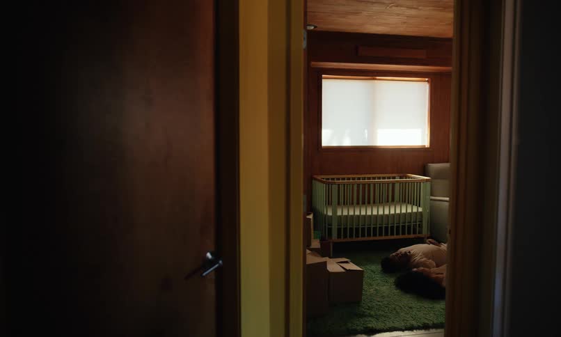 A man and a woman lying on the floor of a partially empty room with a wooden crib set up near the window