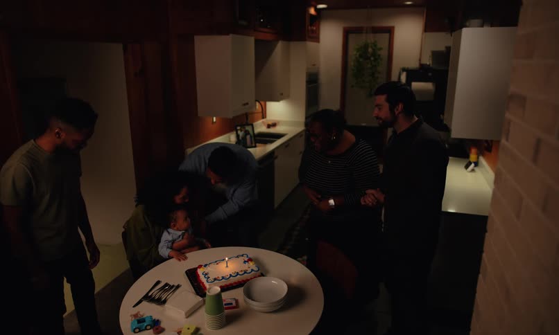 A group of people is around a small child with a birthday cake and candle on the table