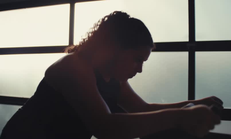 A woman uses a stationary bike in a bright room with large windows