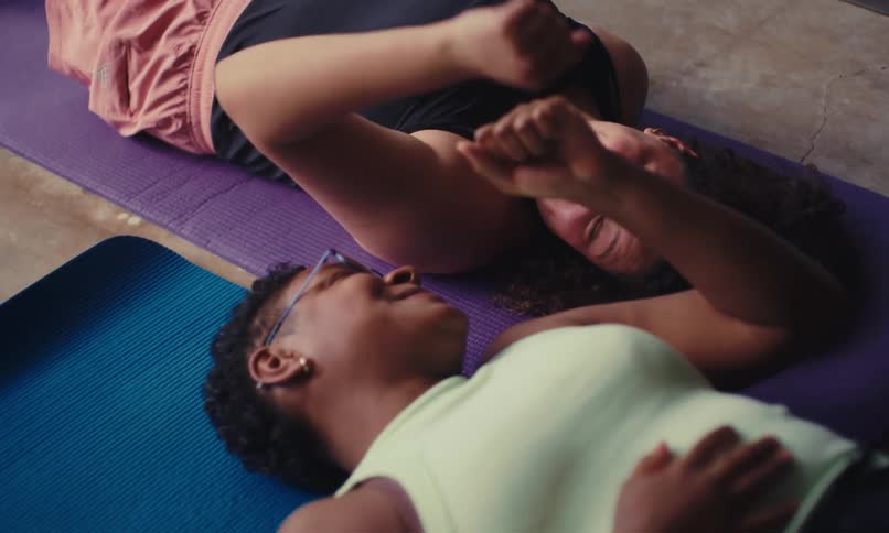 Two women laying down exhausted fist bumping after a workout on yoga mats