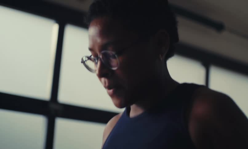 A woman performs cardio exercises jumping in place in a room with large bright opaque windows