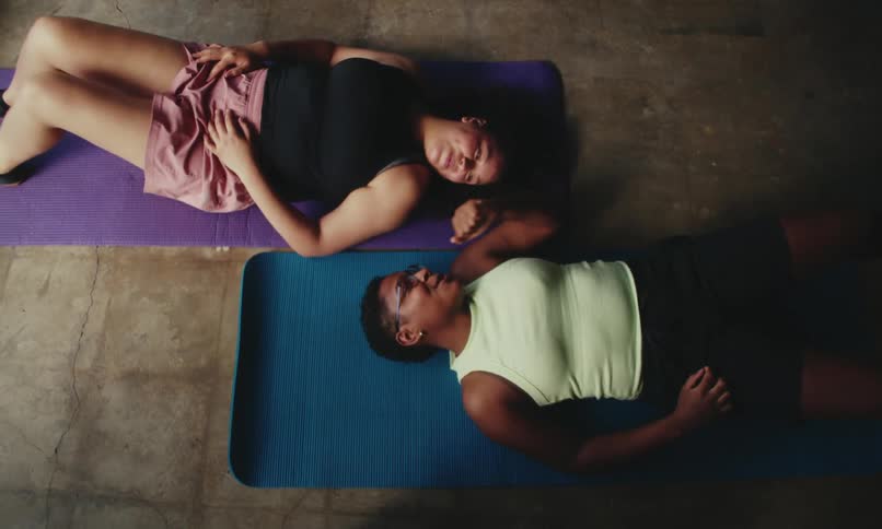 Two women one white and the other black lying on a yoga mat after finishing their exercise for the day giving each other a fist bump