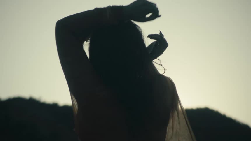 Silhouette of a woman from behind dancing outdoors