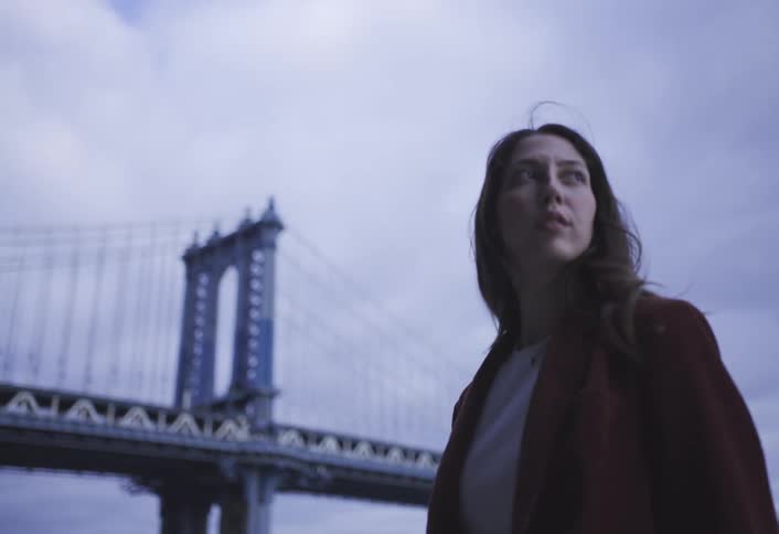 A woman is standing outside in a city near a bridge