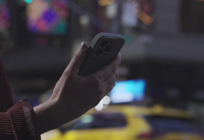 A womans hand holds a smartphone on a busy metropolitan street