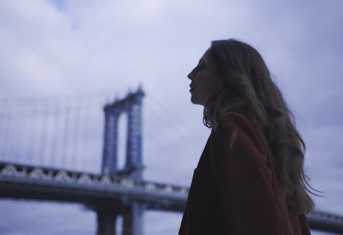 A woman standing near a bridge looks nervous as she looks around
