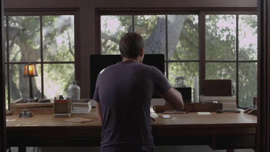 A man works at a computer and sips from a mug