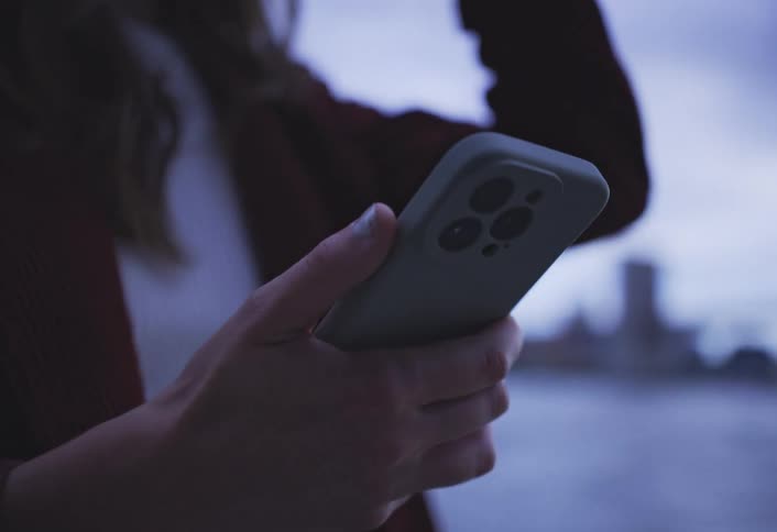 A woman looks at her smartphone while standing near a body of water