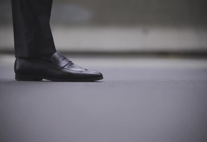 A group of men wearing dress pants and shoes walk on a city sidewalk