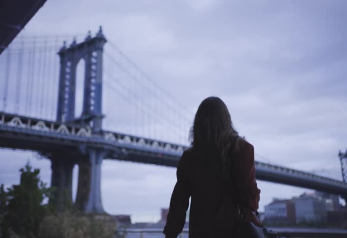 Woman walks toward the manhattan bridge under a cloudy sky