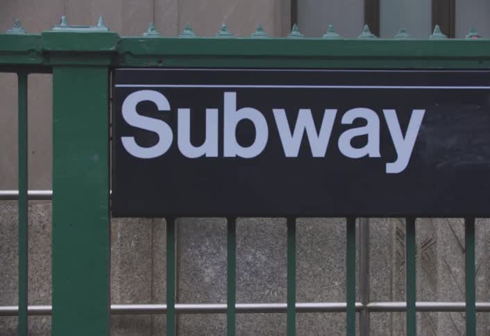 People in a city walk past a subway entrance