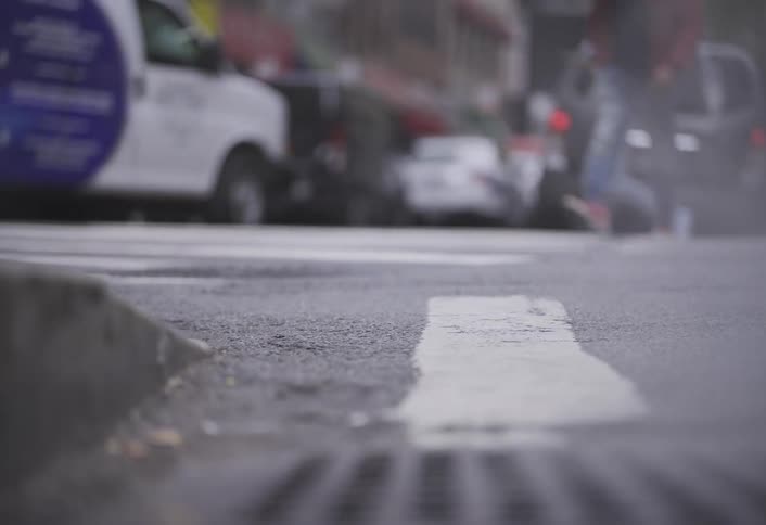 Steam rises from a grate in a city full of pedestrians and vehicles