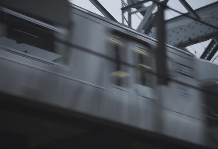Side view of a subway train speeding across a steel bridge with visible motion blur on a cloudy day